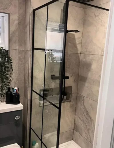 Fitted bathroom shower in Liverpool with black crittall-style glass screen and marble-effect tiling